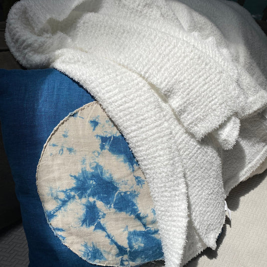 White towel draped over a blue and white tie-dye pillow on a surface.